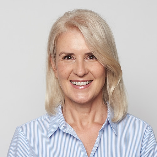 Beautiful 50 years blonde woman is smiling isolated over grey studio wall